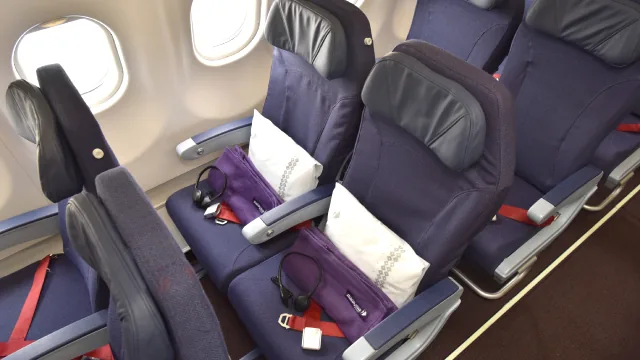 Dua kursi Economy Malaysia Airlines di sisi jendela, lengkap dengan bantal, selimut, dan headphone